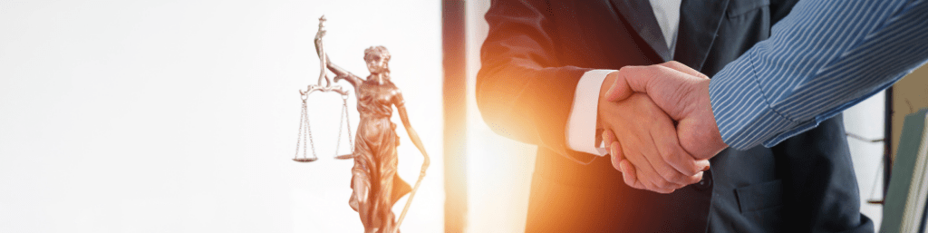 Legal attorney shaking hands with a client in front of a justice statue, symbolising trust, partnership, and professional legal services.