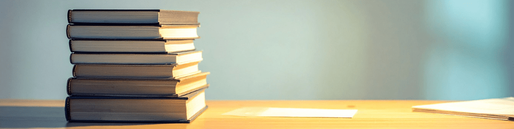 Stack of academic books on a wooden desk representing research and study material for academic transcription services